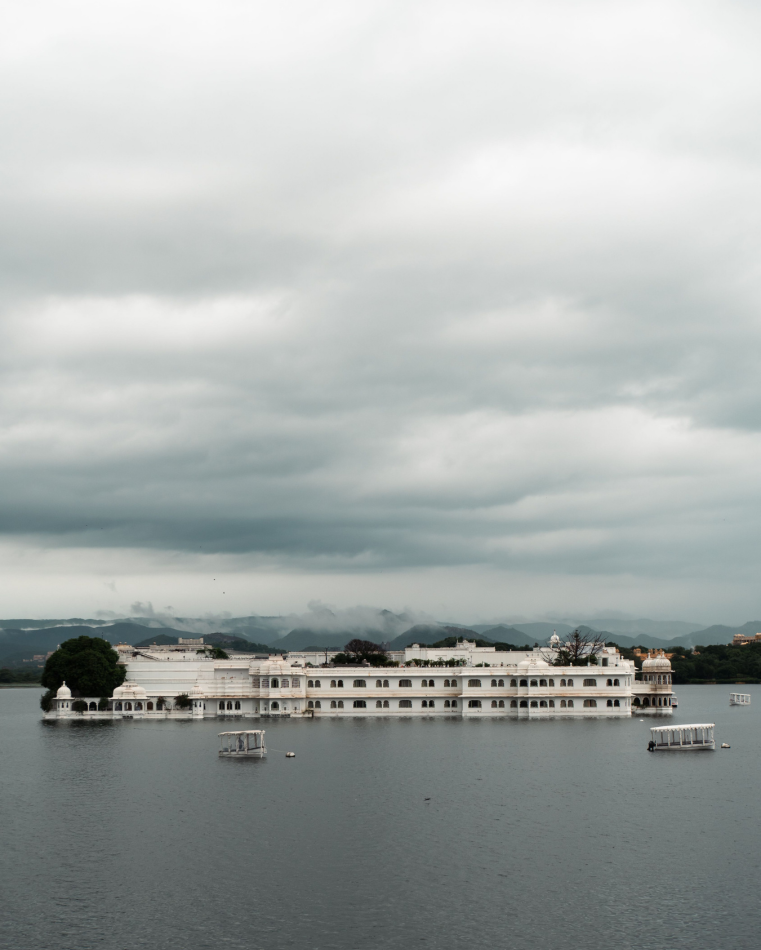 The Taj Lake Palace under the kind of sky that empties Udaipur of its winter crowds. Those low clouds caught on the Aravallis are a sight the dry-season visitor goes home without.